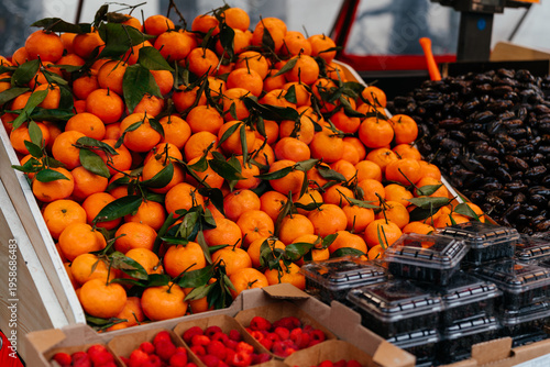 Фотография Fresh mandarins with green stems displayed in a market box alongside organic berries and figs