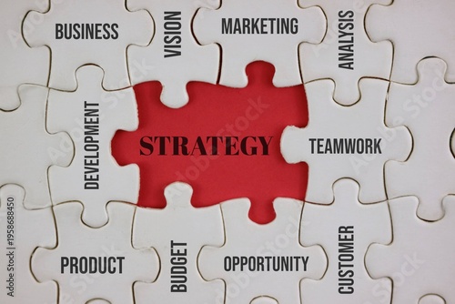a jigsaw puzzle with an red center labeled “Strategy” surrounded by pieces stamped business, marketing, teamwork, development and customer, representing planning, leadership and opportunity.
