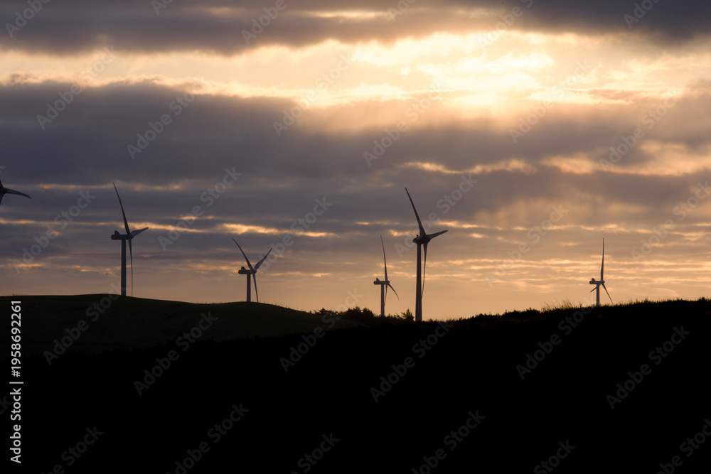 Obraz premium Wind energy turbines silhouetted against a dramatic sunset sky