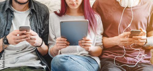 Gadgets addiction. Cropped of young people using smartphones and tablet on couch at home, browsing social media, chatting online, digital lifestyle, mobile technology, communication leisure concept