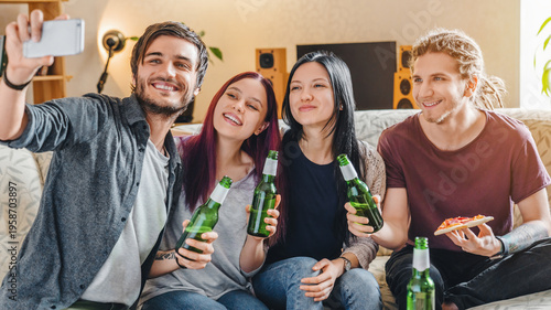 Obraz na plátně Young friends taking a selfie while enjoying pizza and beer at home, sitting on