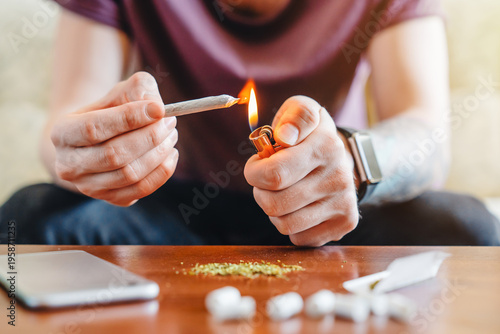Fotografia Close up of man holding cigarette and lighter at home, lighting cigarette, addic