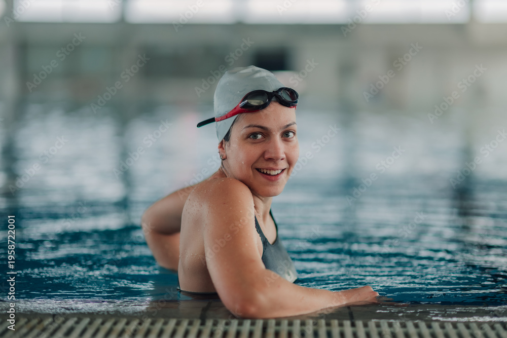 Fototapeta premium Woman wearing a swim cap and goggles, relaxing at the edge of an indoor swimming pool, enjoying sport activity