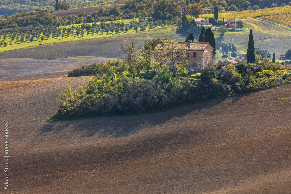 Naklejka premium Tuscan farmhouse surrounded by plowed fields and olive groves, Italy.