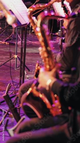 Close-up of a saxophonist performing live on a dark stage. The shallow depth of field creates a beautiful bokeh effect from purple pink stage lights reflecting on the instrument