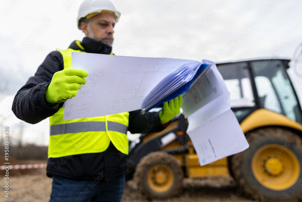 Fototapeta premium Construction supervisor examining blueprints at heavy equipment work site