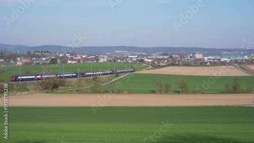 Scenic view with rural landscape and S-Bahn train arriving at Swiss village of Rümlang on a sunny spring afternoon. Video shot March 24th, 2026, Zurich Rümlang, Switzerland.