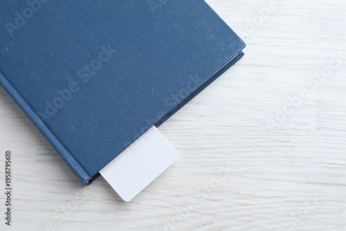 Book with white bookmark on light wooden table, top view. Space for text