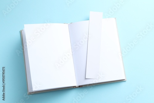 Book with white bookmark on light blue background, top view. Space for text