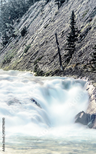Fast moving river in the Rocky Mountains, at the bottom of a cliff.