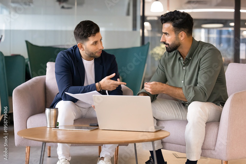 Φωτογραφία Two male colleagues collaborate on task in office lounge, discussing documents or project updates, planning strategy, explaining ideas or solutions during business meeting