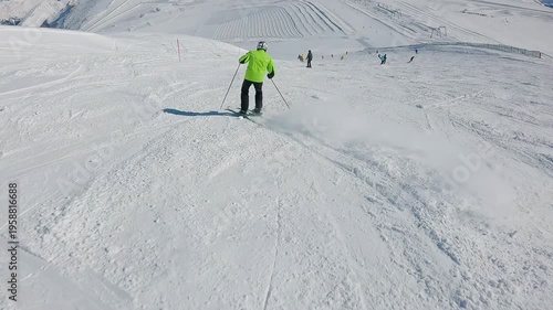 Skier in green jacket descends snowy mountain slope during sunny winter day. Slow motion POV	