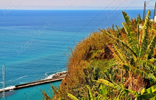 A sunny summer beach with blue ocean waves, sandy shore, and green grass along the coastline in Madeira 