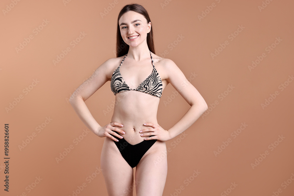 Fototapeta premium Beautiful young woman wearing stylish bikini on brown background