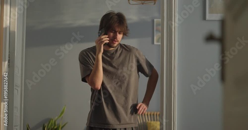 A man stands in a sunlit room, deep in conversation on the phone, sharing moments of joy and curiosity