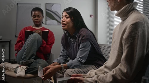 Side view shot of emotional Hispanic woman speaking while sitting on chair during support group meeting for women and sharing life story, copy space