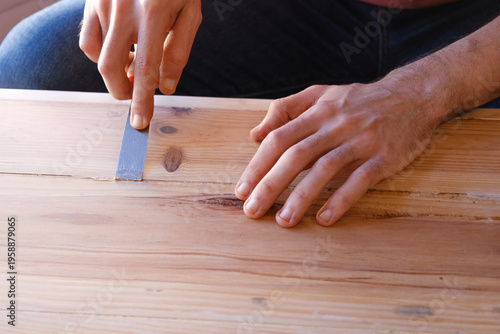 Male hands carefully apply wood filler with a spatula during the restoration of a chest.