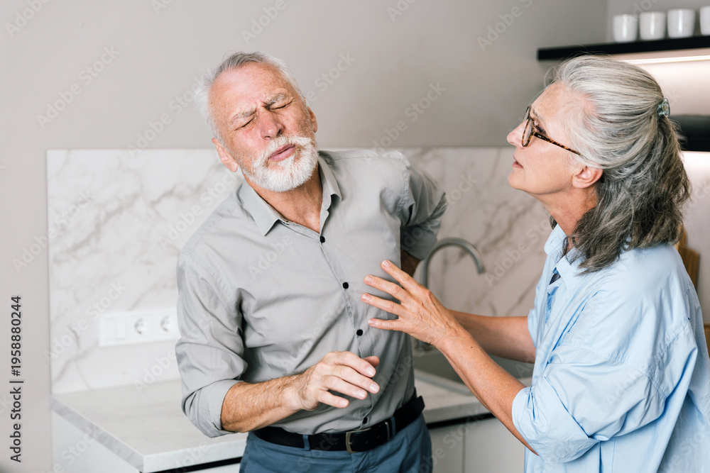 Obraz premium Senior man suffering acute back pain supported by wife in kitchen