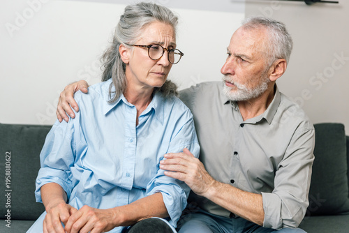 Senior man comforts sad woman during difficult conversation at home