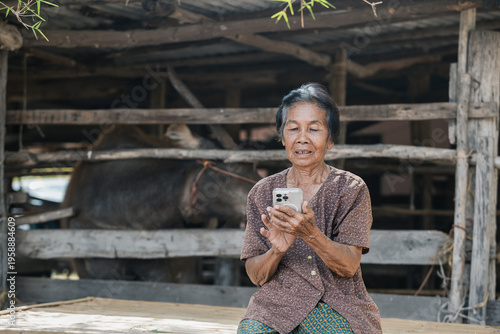 Smiling elderly Asian woman from rural community is happily using her mobile phone.