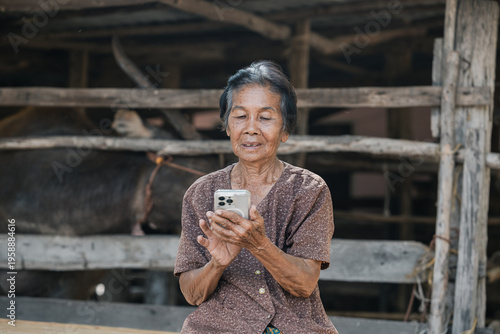 Smiling elderly Asian woman from rural community is happily using her mobile phone.