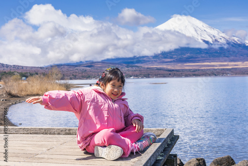 Child happily sitting on a wooden pier overlooking lake yamanakako and mount fuji