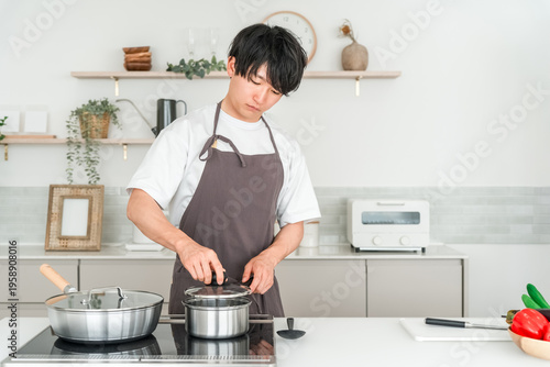 фотографія A young Asian man in an apron cooking in the kitchen (dislike, hate, troublesome