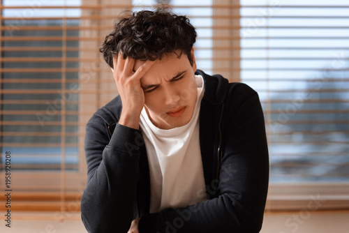 Sad young man near window a...