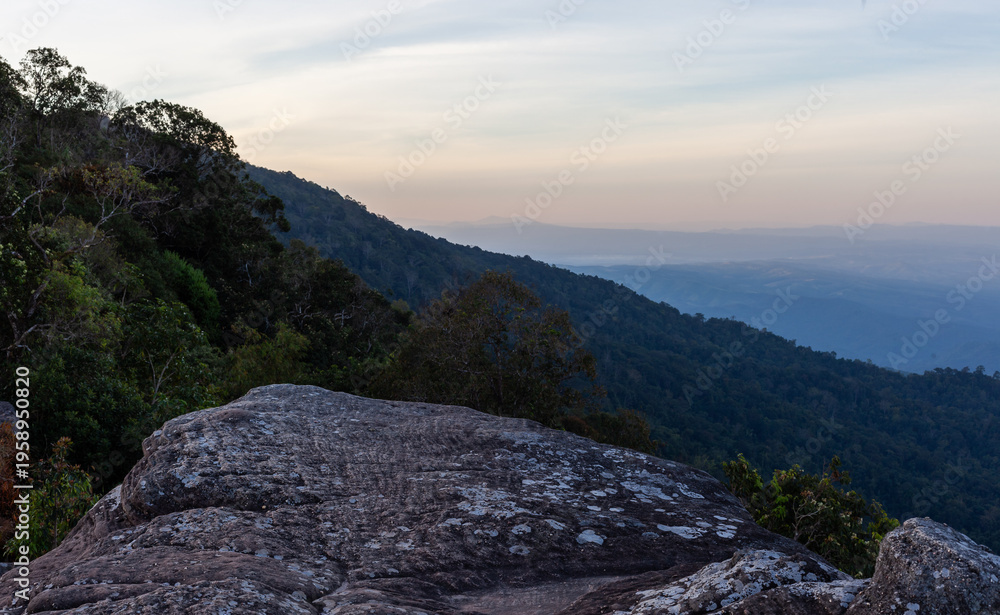 Obraz premium Phu Hin Rong Kla National Park mountain landscape at sunrise. Rugged rocky terrain with forested hills. Hazy sky above a scenic natural view in Thailand.