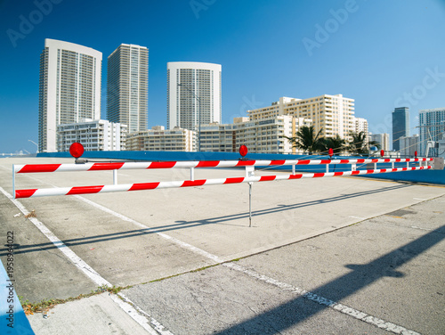 Closed road on a bascule bridge with red and white striped barrier gate and traffic lights against modern skyscrapers in Florida.