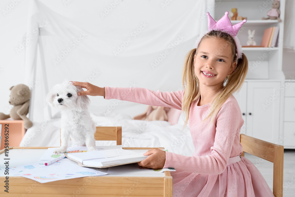 Obraz premium Cute little happy girl with Maltese dog reading book at table in children's bedroom