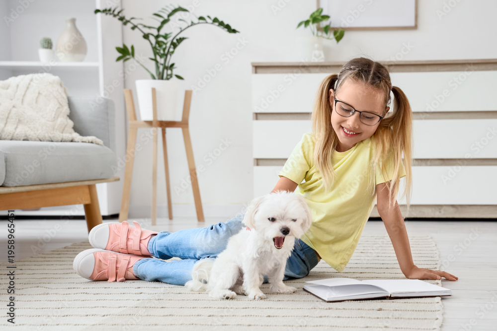 Obraz premium Cute little happy girl with Maltese dog reading book on floor at home