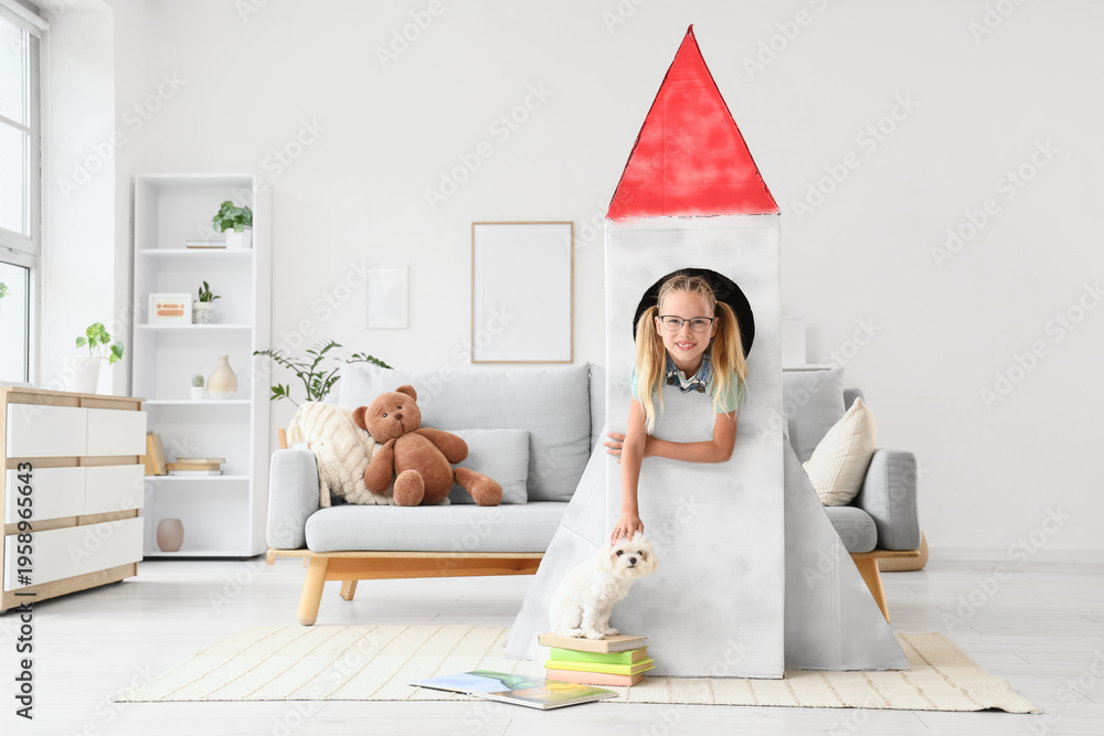 Naklejka premium Cute little happy girl with Maltese dog and books in cardboard space rocket at home