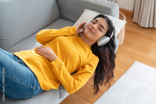 Portrait of Asian woman relaxing listening audio with headphones sitting on a couch at home