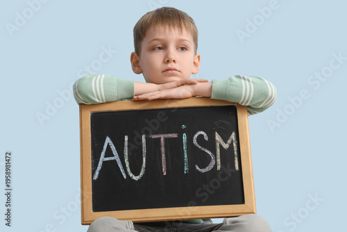 Little boy holding chalkboard with word AUTISM on blue background