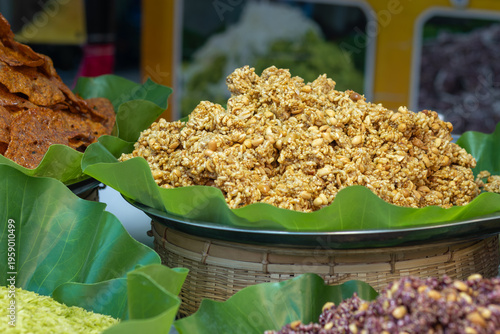 Close-up of a Thai market stall with traditional snacks—caramelized peanuts, crispy crackers, and colorful treats on banana leaves, inviting visitors to taste authentic flavors.