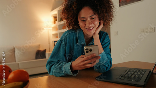 Smiling Woman Using Phone At Home With Laptop