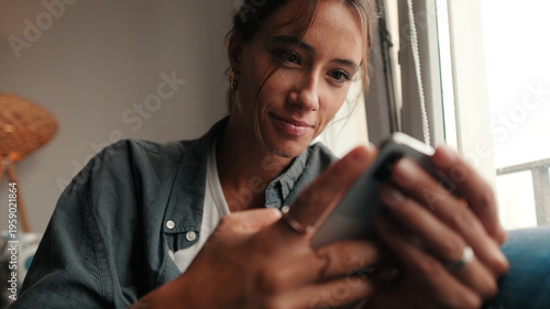 Woman Using Smartphone By Window In Quiet Home