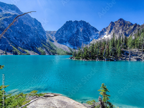 Turquoise lake mirrors jagged mountains under clear blue skies