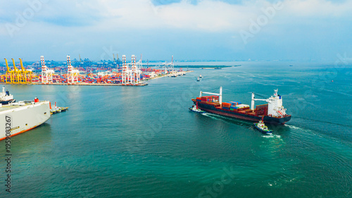 Canvas Print Aerial view of container cargo ship sailing toward busy industrial seaport with cranes and logistics terminals in daytime, global transportation and international shipping industry concept