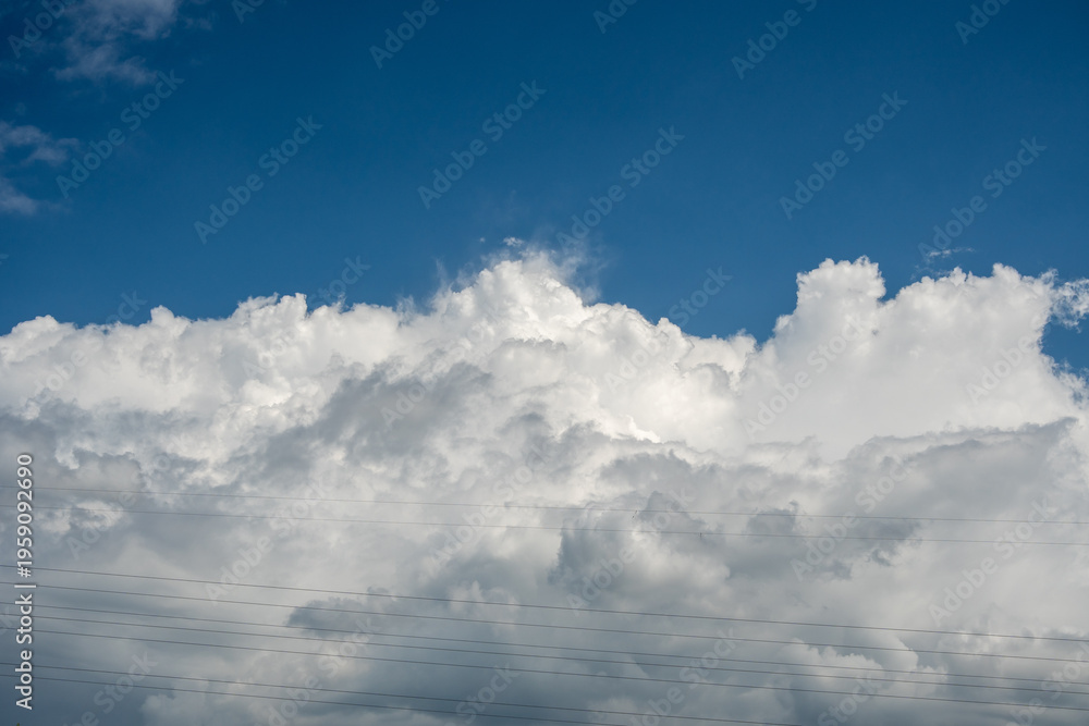 Fototapeta premium Large white cumulus clouds in blue sky behind power lines