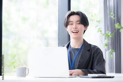 Konstfotografi パソコンに向かう若いビジネスマンカメラ目線　若手社員の爽やかな成長と成功のビジネスシーン