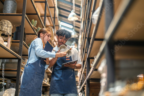 Diverse small business owners in denim aprons checking ceramic mug inventory, Man holding tablet and woman with clipboard managing warehouse stock together, Ecommerce retail teamwork logistics SMEs