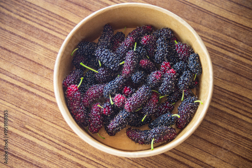 Mulberry fruits in a bowl on wooden table. Top view.