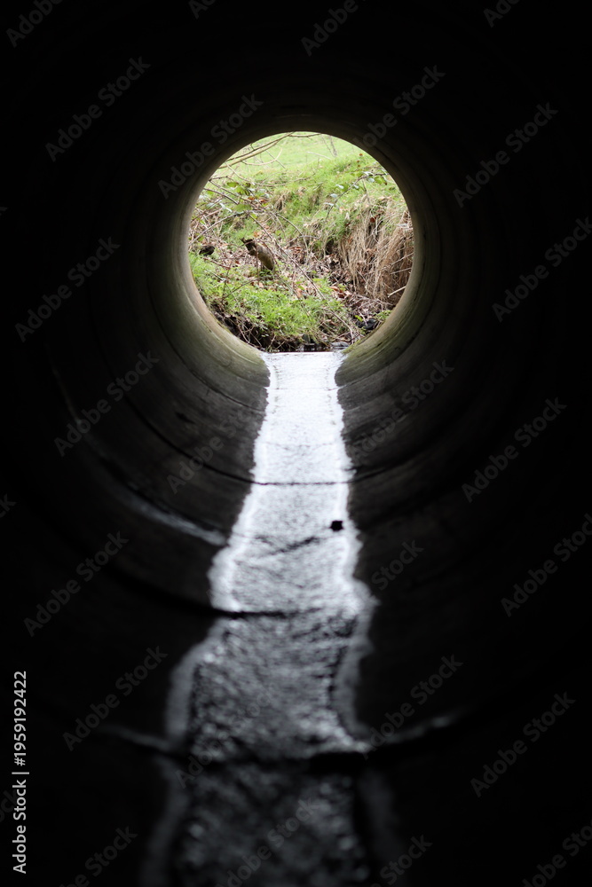 Fototapeta premium View through a round concrete tunnel carrying a stream beneath a road