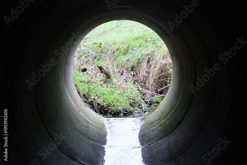 Tableau sur toile View through a round concrete tunnel carrying a stream beneath a road