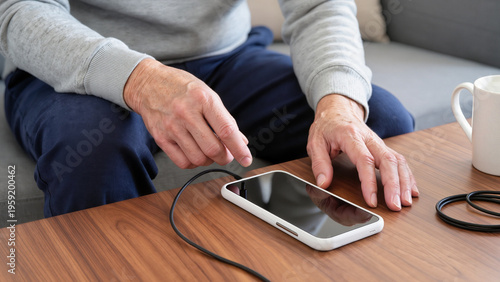 Quadro su tela A senior is charging a smartphone, The elderly man holds a mobile device, A gran