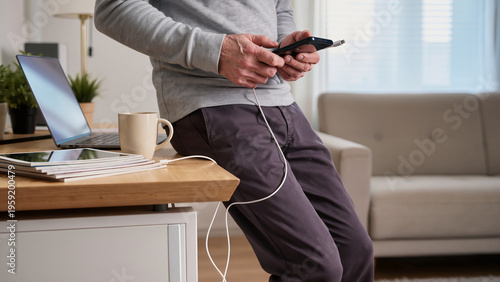 A senior is charging a smartphone, The elderly man holds a mobile device, A grandfather is plugging in a phone, He connects the charger to the port, The senior manages modern technology at home