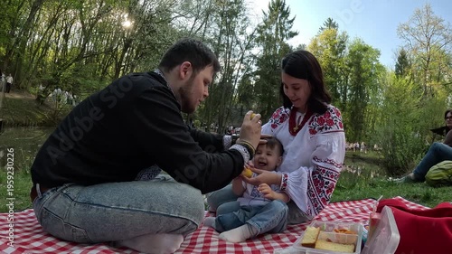 Family picnic feeding baby on red checkered blanket