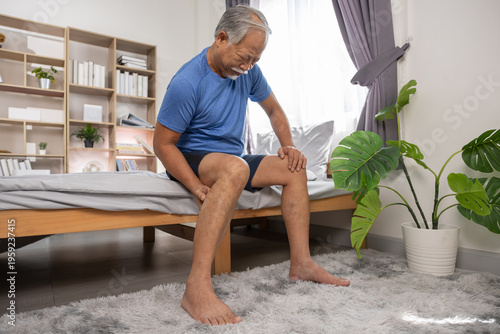 Foto Senior asian man sitting on comfortable bed feeling severe leg muscle pain and j